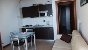 A compact kitchen with a dining area, a sofa, and a door leading to another room.