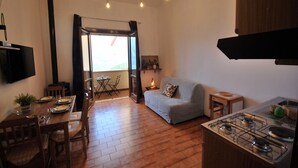 A compact living space with a dining area, a sofa, a kitchen with a gas stove, and a view through a glass door. - Nadia by Theater Home, with garden and marvellous lake view (Tignale)