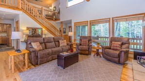 A spacious living room with a wooden staircase, large windows, and a cozy fireplace. - ACER04 - Spacious Home, Hot Tub, Fireplace, Ping Pong, Foosball (Sunriver)