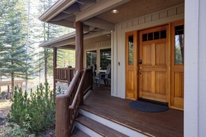 Une véranda en bois à l’avant de la maison, avec un escalier menant à une porte, le tout entouré d’arbres.