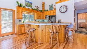 A spacious kitchen with wooden cabinets, a central island with bar stools, and a large window. - ACER04 - Spacious Home, Hot Tub, Fireplace, Ping Pong, Foosball (Sunriver)