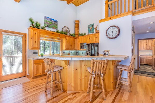 A spacious kitchen with wooden cabinets, a central island with bar stools, and a large window. - ACER04 - Spacious Home, Hot Tub, Fireplace, Ping Pong, Foosball (Sunriver)