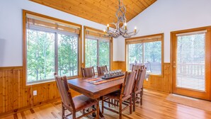 A dining area with a wooden table and chairs, large windows, and a chandelier. - ACER04 - Spacious Home, Hot Tub, Fireplace, Ping Pong, Foosball (Sunriver)