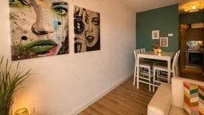 Una sala de estar con un sofá blanco, una mesa de comedor con sillas y dos grandes cuadros abstractos en la pared.