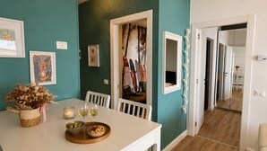 Un comedor con una mesa blanca, sillas y suelo de madera. Hay una puerta que conduce a otra habitación.