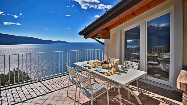 Une terrasse avec une table dressée pour le repas, offrant une vue sur un plan d’eau et des montagnes.