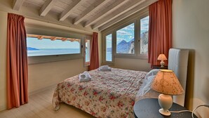 Une chambre à coucher avec un lit, une table avec une lampe et une vue sur la mer grâce à de grandes fenêtres.