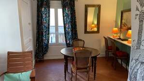 A dining area with a round table, four chairs, a window with curtains, a mirror, and two lamps on a shelf. - Duplex apartment (two people) (Dieppe)