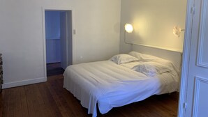 A bedroom with a bed, wooden flooring, a white door, and a light fixture on the wall. - Duplex apartment (two people) (Dieppe)