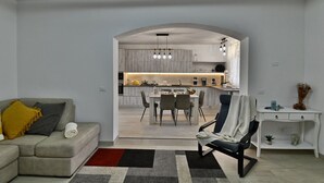 Un salon moderne avec un canapé, un coin repas comprenant une table et des chaises, et une cuisine visible à travers une arche.