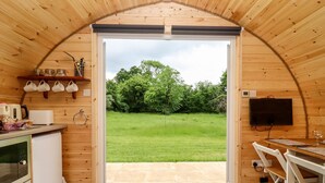 A cozy wooden cabin with a kitchen area, a dining table, and a large sliding glass door leading to a grassy yard. - Meadow Lodge @ Berrys Place Farm (Gloucester)