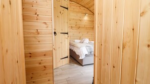 A wooden room with a bed, a door, and a light fixture on the ceiling. - Meadow Lodge @ Berrys Place Farm (Gloucester)