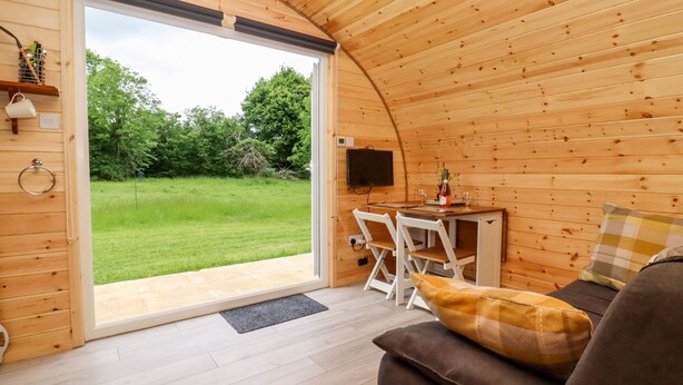 A cozy, wooden interior with a dining area, a sofa, and a large window offering a view of a grassy outdoor area. - Meadow Lodge @ Berrys Place Farm (Gloucester)