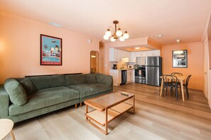 A living room with a sofa, a coffee table, a dining area with a table and chairs, a kitchen with appliances, and a ceiling light fixture. - 136 · ☀Pool✔ Kitchen✔ Beach✔ Self Check-In✔ Parking✔ (Clearwater)