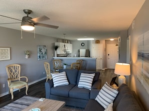 A modern living room with a gray sofa, wooden chairs, a coffee table, and a ceiling fan.