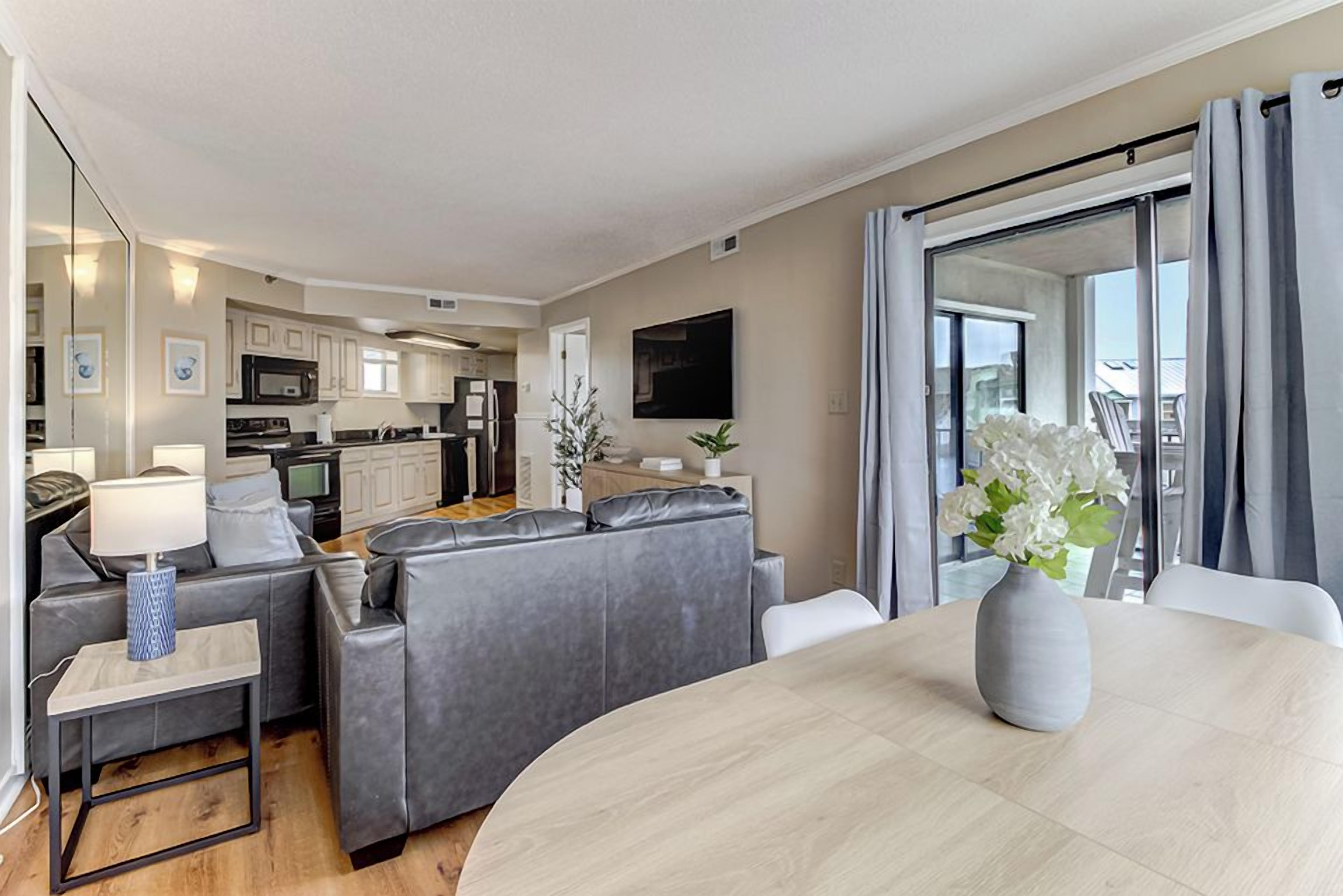 A modern living room with a sofa set, a dining table, and a kitchen in the background.