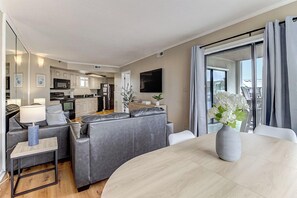 Una sala de estar moderna con un conjunto de sofás, una mesa de comedor y una cocina al fondo.