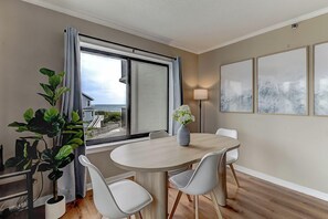 Un comedor con una mesa redonda, sillas blancas, una planta en maceta y vistas al mar a través de un ventanal grande.