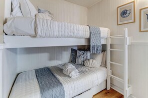 Ein Stockbett mit weißem Kopfteil und einem unterem Bett mit gesteppter Decke.