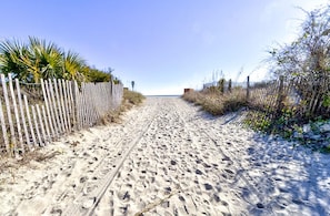 A sandy path leading to a beach, flanked by a wooden fence and vegetation. - Ocean Views, Balcony, Pool, STEPS to Beach Restaurants Shops (Wrightsville Beach)