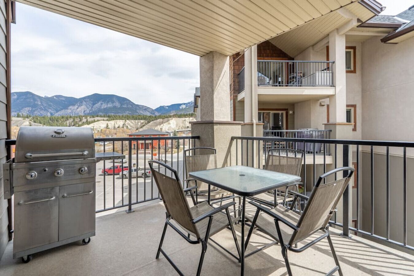 En balkon med grill, bord og stole, der giver udsigt over et bjergrigt landskab.