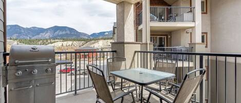 Un balcon doté d’un barbecue, d’une table et de chaises, offrant une vue sur un paysage montagneux.