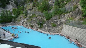Ein großer Außenpool mit mehreren Bahnen, umgeben von einer felsigen Klippe und viel Grün.
