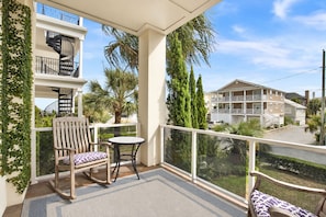 A balcony with a wooden rocking chair and a small table, overlooking a residential area with houses and palm trees.