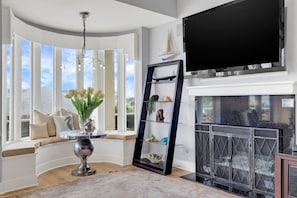 A living room with a large window, a fireplace, and a flat-screen TV mounted above it.