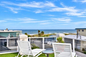 Ein Balkon mit weißen Stühlen und einem Tisch mit Blick auf einen Strand und den Ozean.