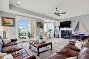 A spacious living room with leather sofas, a coffee table, a fireplace, a sailboat model, and a television.