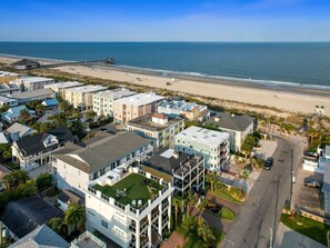 Un quartier résidentiel situé sur la côte, avec des propriétés donnant sur la plage, notamment un grand immeuble doté d’un jardin sur le toit et d’une jetée s’avançant dans l’océan.