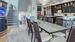 Une cuisine moderne avec des meubles de couleur sombre, des appareils en acier inoxydable et une table à manger en verre, assortie de chaises.