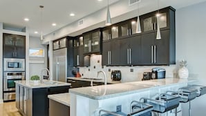 Une cuisine moderne avec des meubles de couleur sombre, des appareils en acier inoxydable et un îlot central doté de tabourets de bar.