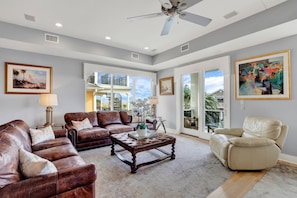 A spacious living room with leather sofas, a coffee table, and artwork on the walls. - Roof Top Deck w/ Ocean Views, Heated Pool Access (Tybee Island)