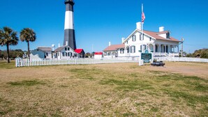 A historic lighthouse with a white and black tower, a white picket fence, and a building with a porch. - Roof Top Deck w/ Ocean Views, Heated Pool Access (Tybee Island)