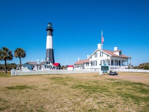 A historic lighthouse with a white and black tower, a white picket fence, and a building with a porch. - Roof Top Deck w/ Ocean Views, Heated Pool Access (Tybee Island)