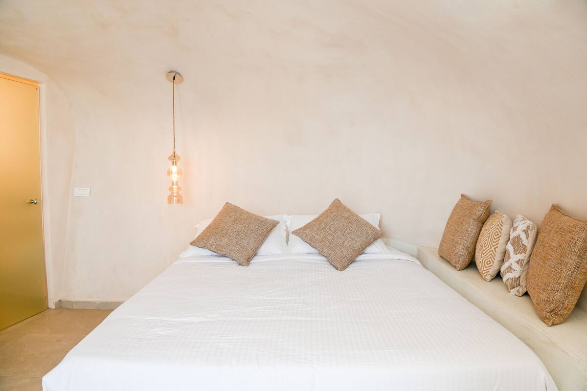 A bedroom with a large bed, a hanging light fixture, and several pillows.