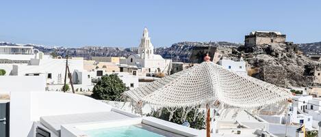En tagterrasse med pool, bord og stole, der kigger ud over et bybillede med hvide bygninger og en fjerntliggende bakke.