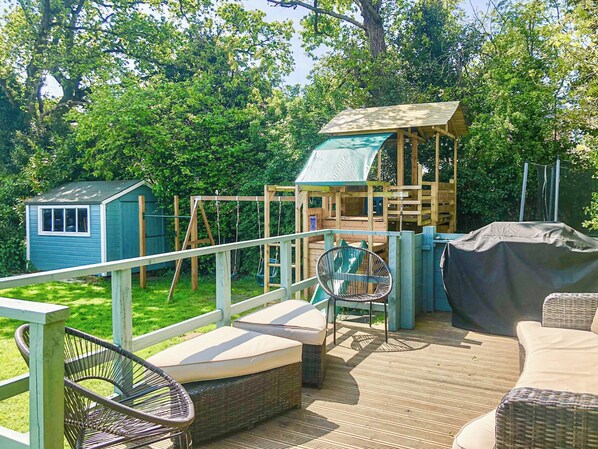 A wooden play structure with a slide, a small shed, and outdoor seating with cushions.