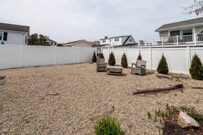 Enjoy the serene atmosphere of this backyard with a gravel surface, white fence, and two coniferous trees.
