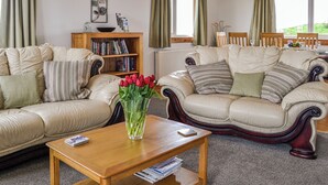 A living room with two beige sofas, a wooden coffee table, a bookshelf, and a vase of red tulips.