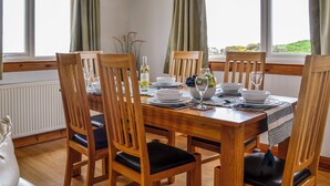 A dining room with a wooden table set for four, surrounded by chairs, and large windows with curtains.