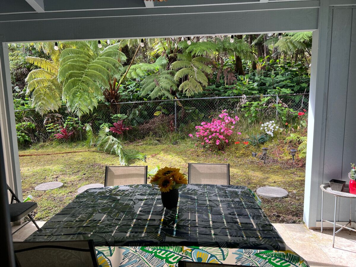 An outdoor patio with a table and chairs, surrounded by lush greenery and a variety of plants.