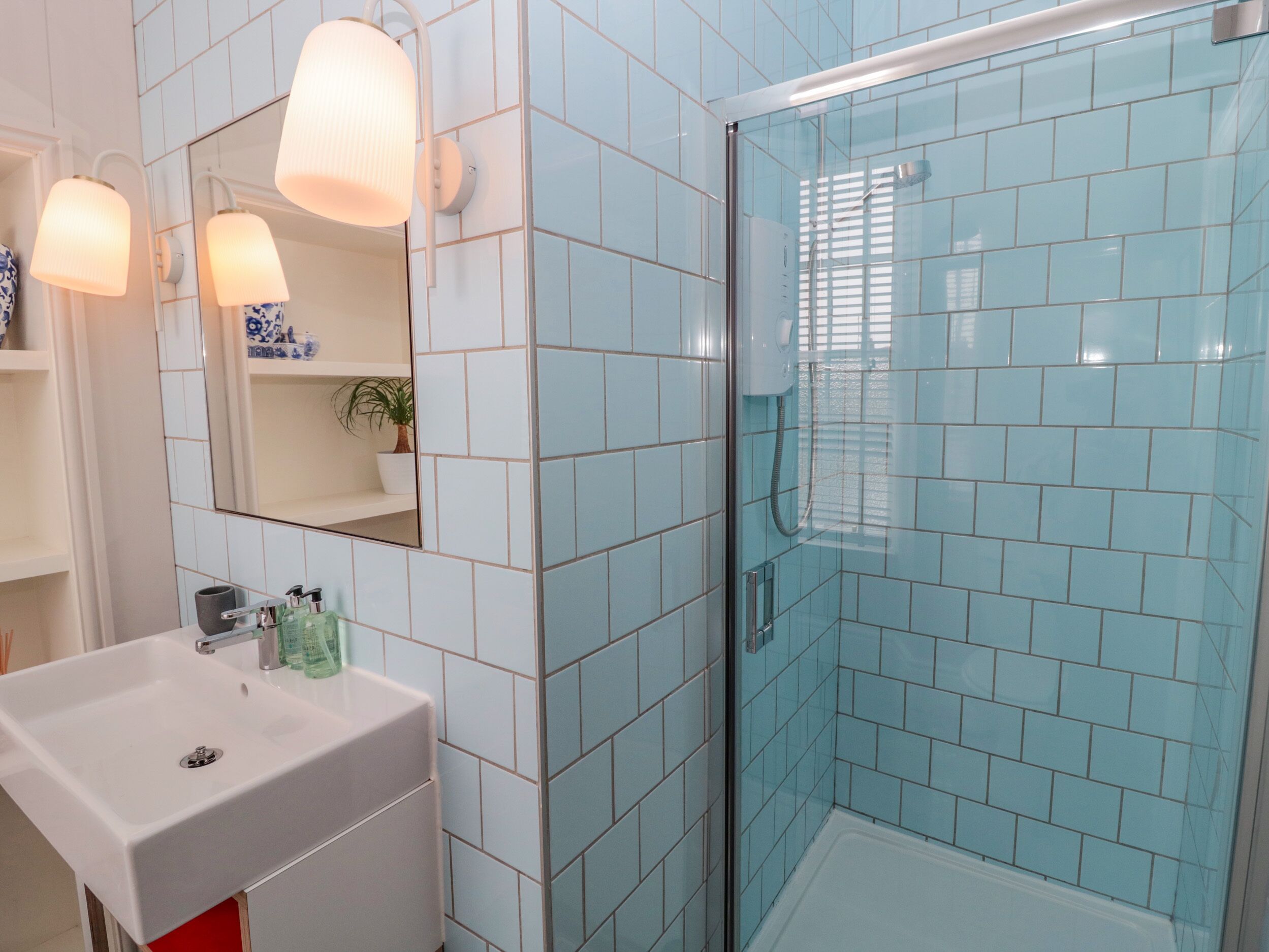 A bathroom with a white sink, a mirror, and a shower with blue tiles.
