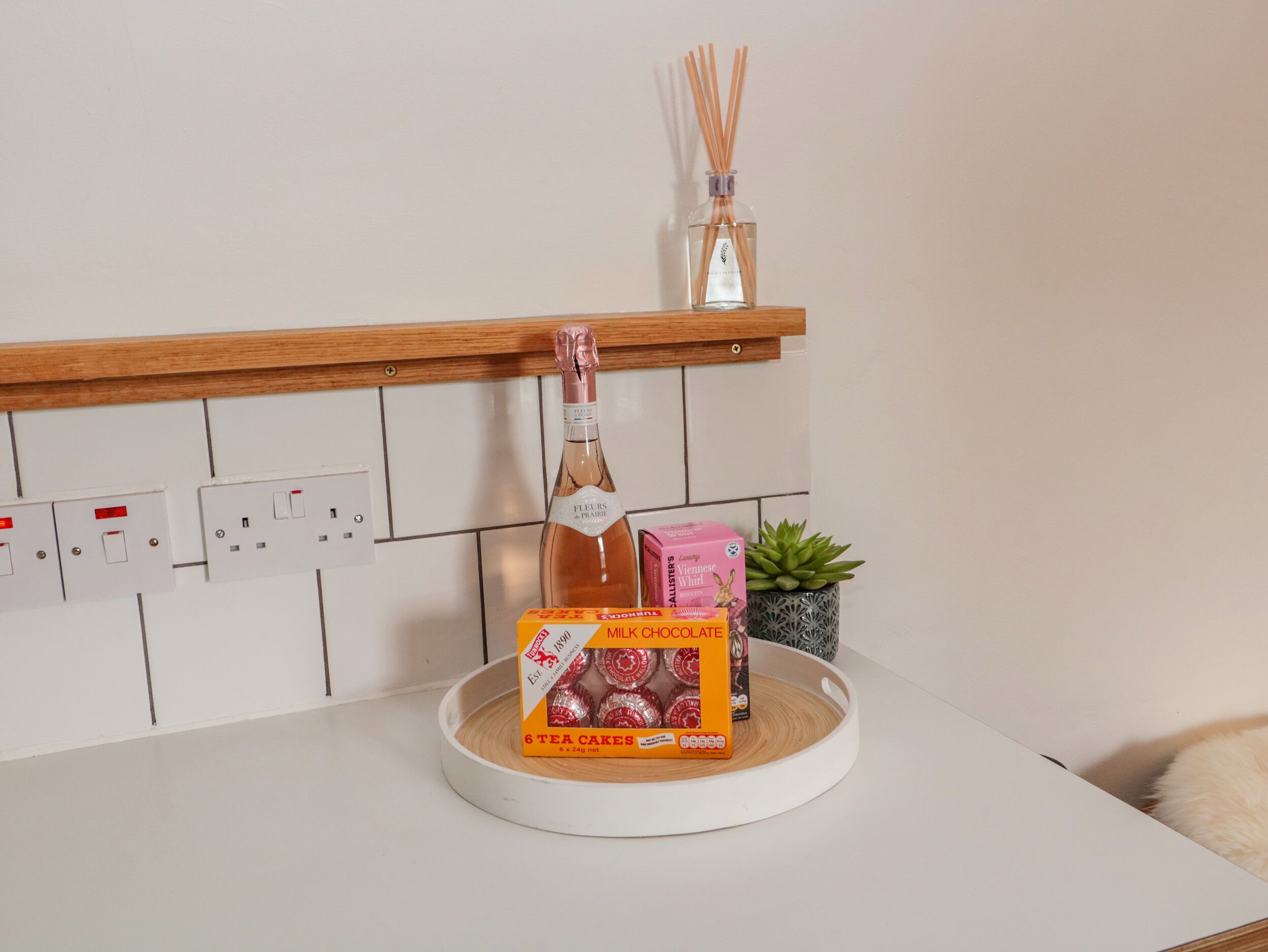 A kitchen counter with a bottle of champagne, a box of tea cakes, and a small potted plant.