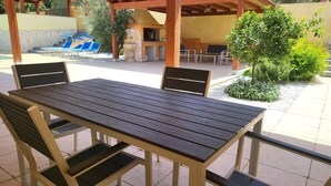 Eine Terrasse im Freien mit Holztisch und -stühlen, einem Grill und einem Poolbereich.