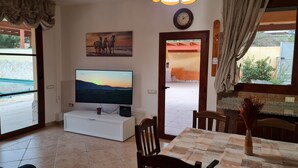 Ein Wohnzimmer mit Flachbildfernseher, einem Esstisch, Stühlen, einer Couch und einem Gemälde an der Wand.