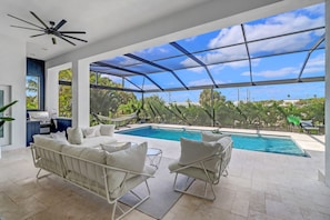 Relax in this open-plan living space with a stunning pool view, comfortable seating, and a grill.