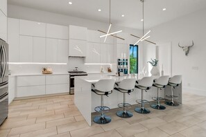Une cuisine moderne avec des meubles blancs, un îlot central doté de tabourets et des luminaires suspendus.